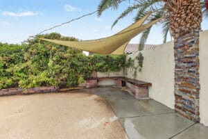 Shaded backyard seating nook with shade sail, built-in wood bench and stacked-stone column