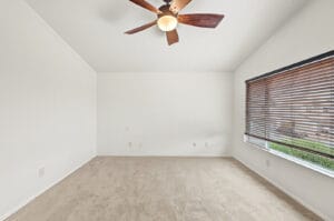 Vaulted bedroom with ceiling fan, wood blinds and neutral carpet