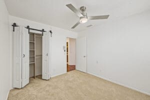 Bedroom with barn-door style closet, ceiling fan and neutral carpet