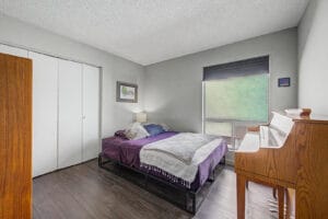 Bedroom with wood-look flooring, double closet, and large window with cellular shade