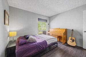 Bedroom with gray walls, wood-look flooring, and window, shown with bed, piano, and guitar