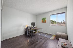Bright bedroom used as a home office, with wood-look flooring and street-facing window