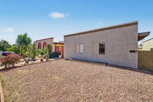 Street-side view of single-story stucco home with gravel landscaping and neighboring desert plantings