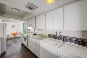 Galley kitchen with white cabinets, electric range, and in-kitchen washer and dryer, looking toward the dining nook