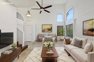 Virtually staged two-story living room with sofas, wood staircase and arched windows