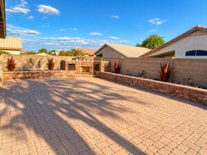 Large paver patio backyard in Peoria, AZ with stone raised planters and a corner outdoor fireplace