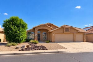 Front of single-story Peoria, AZ home with tile roof, arched entry, three-car garage and desert landscaping