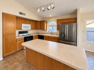 Kitchen with oak cabinets, large island, stainless French-door refrigerator and arched window over the sink